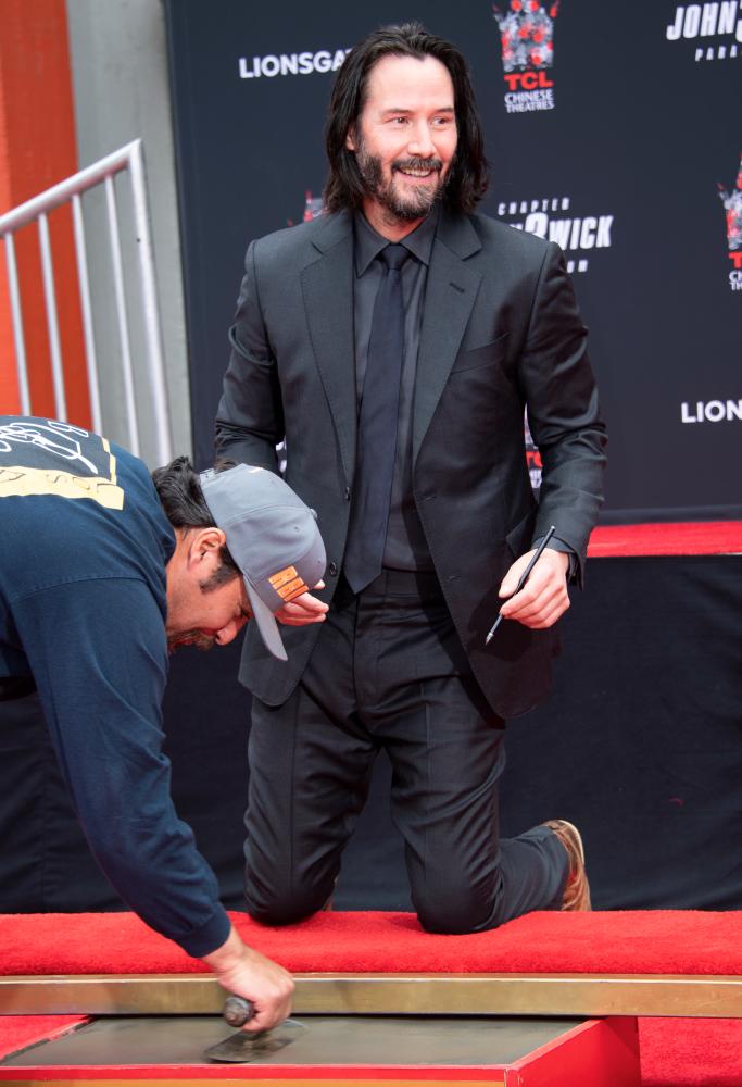 Actor Keanu Reeves signs his name in cement during his handprint ceremony at the TCL Chinese Theatre IMAX forecourt