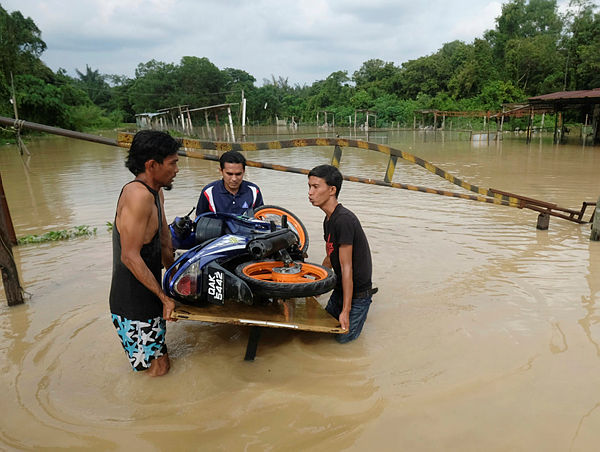 Three teens carry a motorcycle on a table to stop it from submerging at nearby Melaka Pindah, Alor Gajah, today.