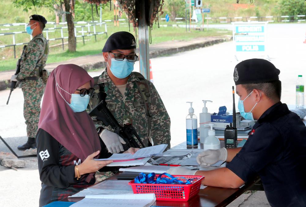 $!Strict CONTROLS ... A resident of Ambangan Heights in the Kenanga Zone in Aman Jaya, one of the three areas placed under enhanced movement control order in Kedah since Aug 28, shows a medical treatment appointment letter to a policeman at a roadblock at Lebuh Kenanga yesterday. - MASRY CHE ANI/THESUN