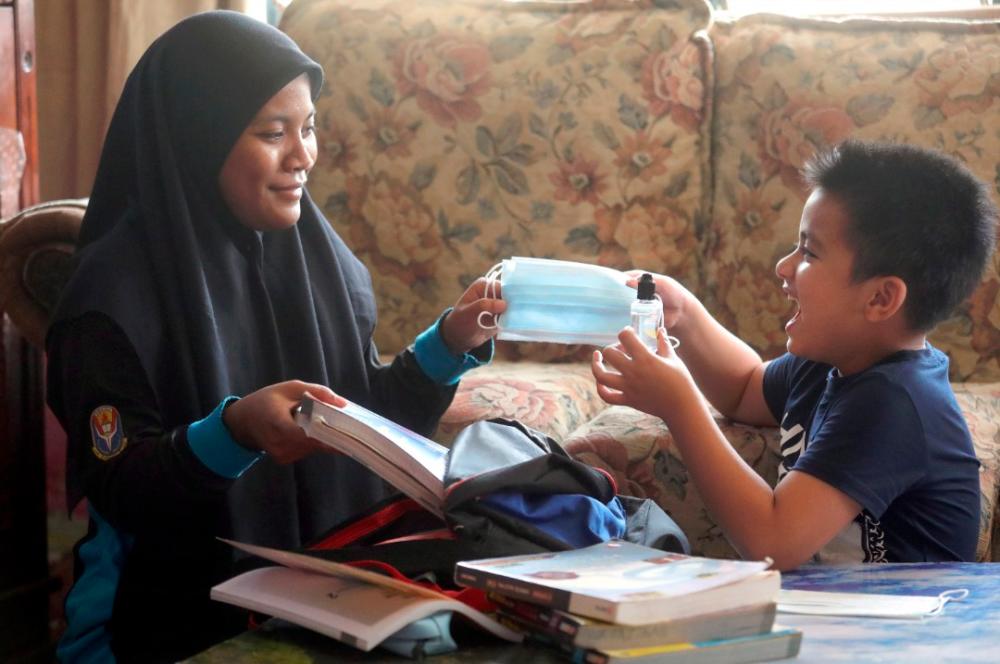Muhammad Irfan Mohd Harmizi, six, handing a face mask and a bottle of hand sanitiser to his cousin Nur Aisyah Mohd Rosdi, 19, who will be resuming classes at Sekolah Menengah Teluk Air Tawar in Penang on Oct 4.