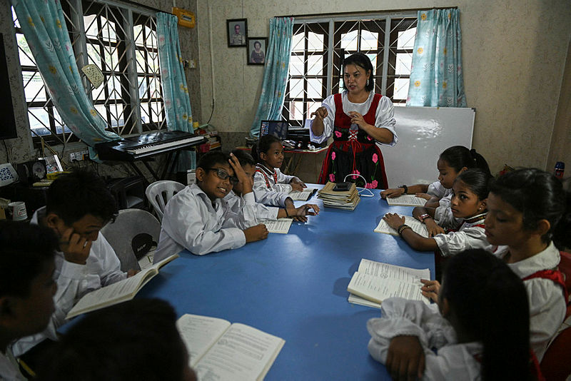 This picture taken on May 11, 2019 shows Sara Santa Maria, 50, teaching students the Kristang language at the Portuguese Settlement in Ujong Pasir, Malacca. Children in colourful outfits sing in a creole of Portuguese and Malay during a class in the historic Malaysian city of Malacca, part of efforts to stem the decline of the centuries-old language. — AFP