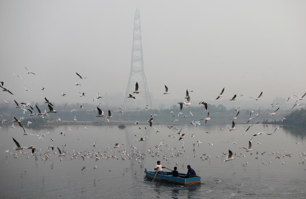 People ride a boat across Yamuna river on a smoggy morning in the old quarters of Delhi, India on Nov 11, 2019. — Reuters