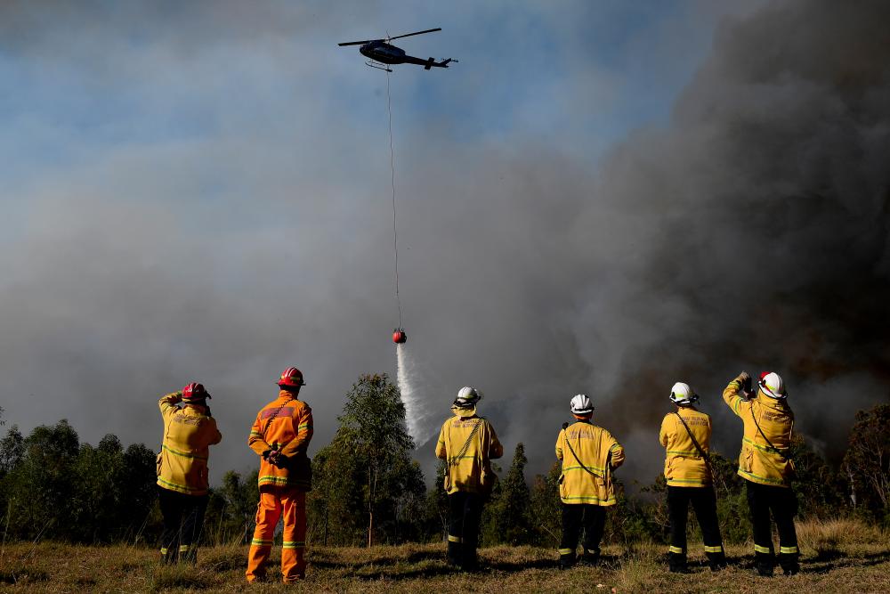 NSW Rural Fire Service crews watch on as a helicopter drops water on to protect properties on Wheelbarrow Ridge at Colo Heights, north west of Sydney, Australia, Nov 19. — Reuters