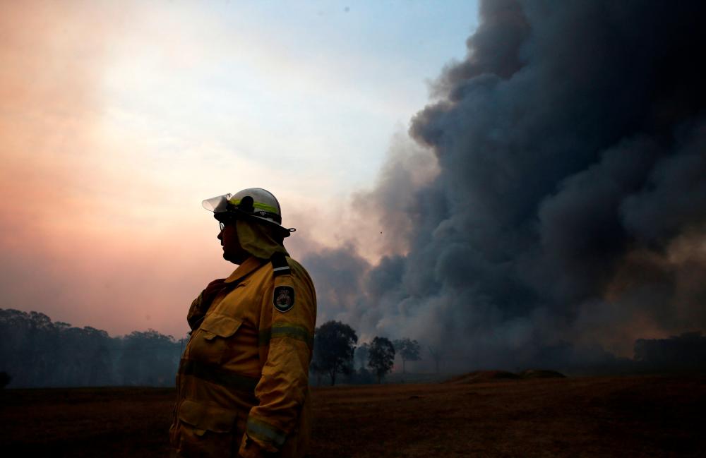 A firefighter talks on a radio as an out-of-control bushfire burns at Avery's Lane, Australia, Dec 3, 2019. — Reuters