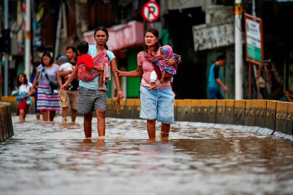 Women carrying their children walk accross the floodwaters at the Jatinegara area after heavy rains in Jakarta, Indonesia, Jan 2. — Reuters