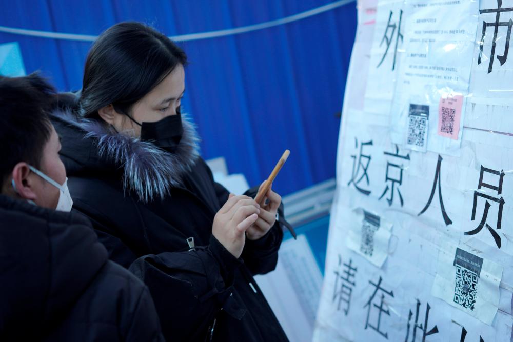 People wearing face masks scan a QR code to submit their information as they return to Beijing, at an entrance of a residential compound, as the country is hit by a novel coronavirus outbreak in Beijing, China on Mar 1. — Reuters