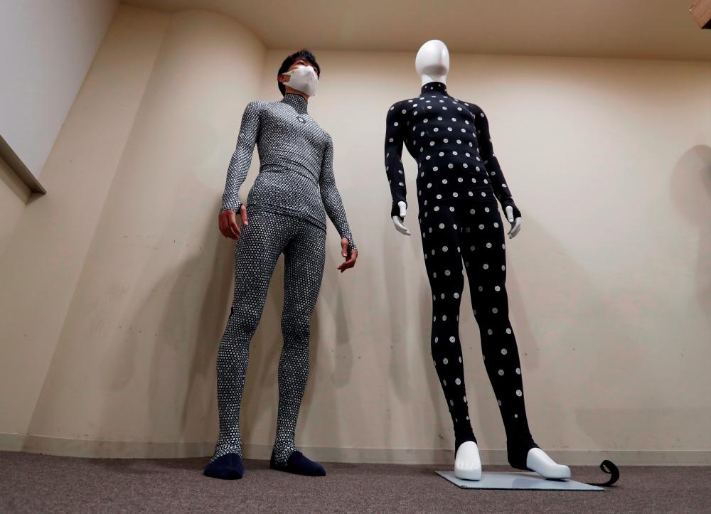 An employee of online fashion retailer Zozo Inc. wearing the company’s Zozosuit 2, a 3D body measurement suit, poses for a photograph next to the previous model of Zozosuit at their Tokyo office in Tokyo, Japan October 30, 2020. Picture taken October 30, 2020. REUTERS/Issei Kato