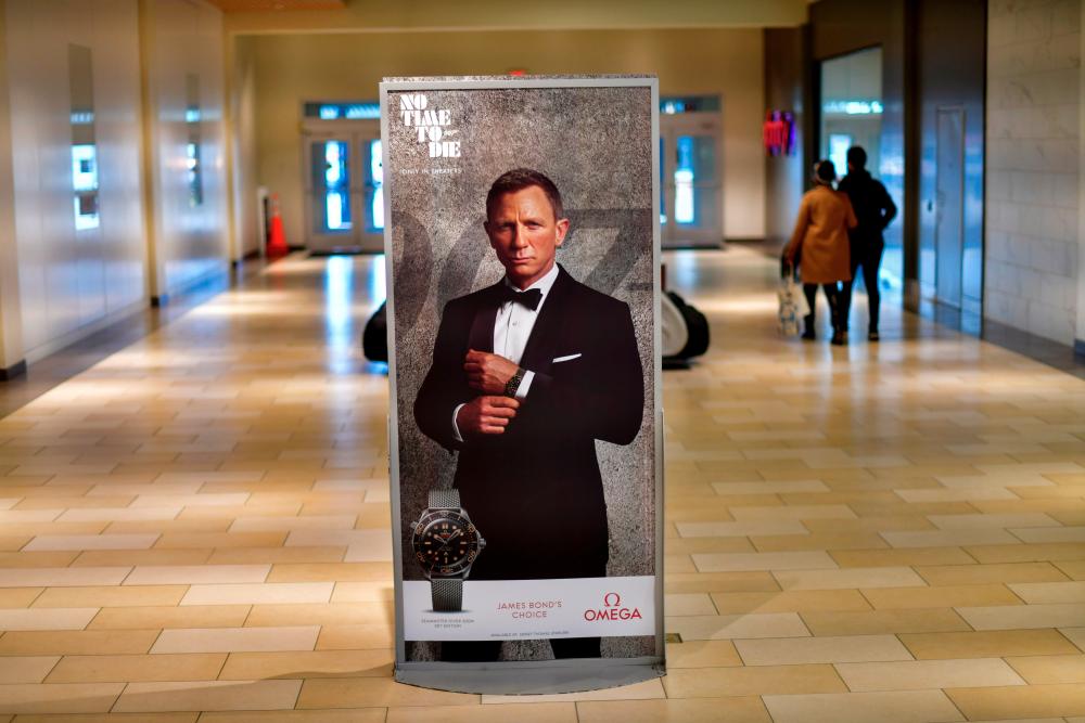 FILE PHOTO: Shoppers walk past an advertisement for the upcoming James Bond film “NO TIME TO DIE” whose release has been delayed to October, at the Christiana Mall in Newark, Delaware U.S. November 19, 2020. REUTERS/Mark Makela/File Photo