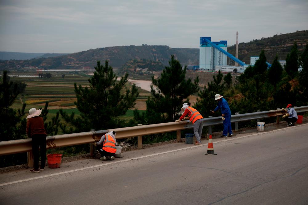 FILE PHOTO: Workers wipe dust off road barriers near the Walnut Valley coal mine that is part of Huaneng Group’s integrated coal power project, near Qingyang, Ning County, Gansu province, China, September 19, 2020. - Reuters