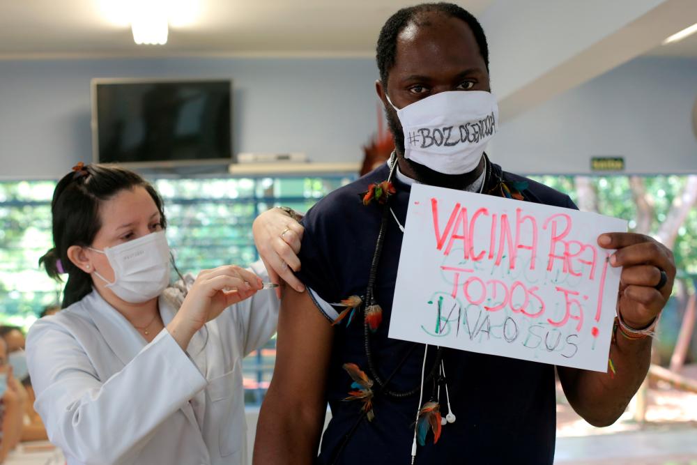 An Indigenous man receives the second dose of Sinovac’s CoronaVac coronavirus disease (COVID-19) vaccine at a health station, as he holds a cardboard that reads: ‘’Vaccine for all now’’ and wears a protective face mask that reads: ‘’#BozoGenocidal’’ in reference of Brazil’s President Jair Bolsonaro, in Guarulhos, near Sao Paulo, Brazil March 2, 2021. - Reuters