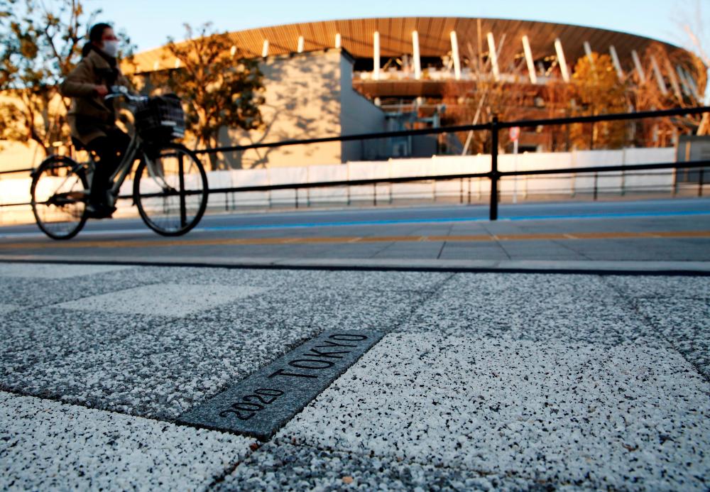 FILE PHOTO: A woman cycles past a sign for Tokyo 2020 Olympic Games on the pavement in front of the National Stadium, the main stadium of Tokyo 2020 Olympics and Paralympics, amid the coronavirus disease (COVID-19) outbreak in Tokyo, Japan, February 3, 2021. - Reuters