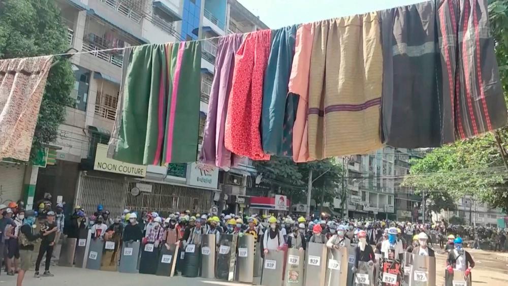 Traditional clothes hang on a rope as protesters holding shields stand in line in the background during a protest against the military coup in Yangon, Myanmar March 6, 2021 in this still image obtained by Reuters from a video.