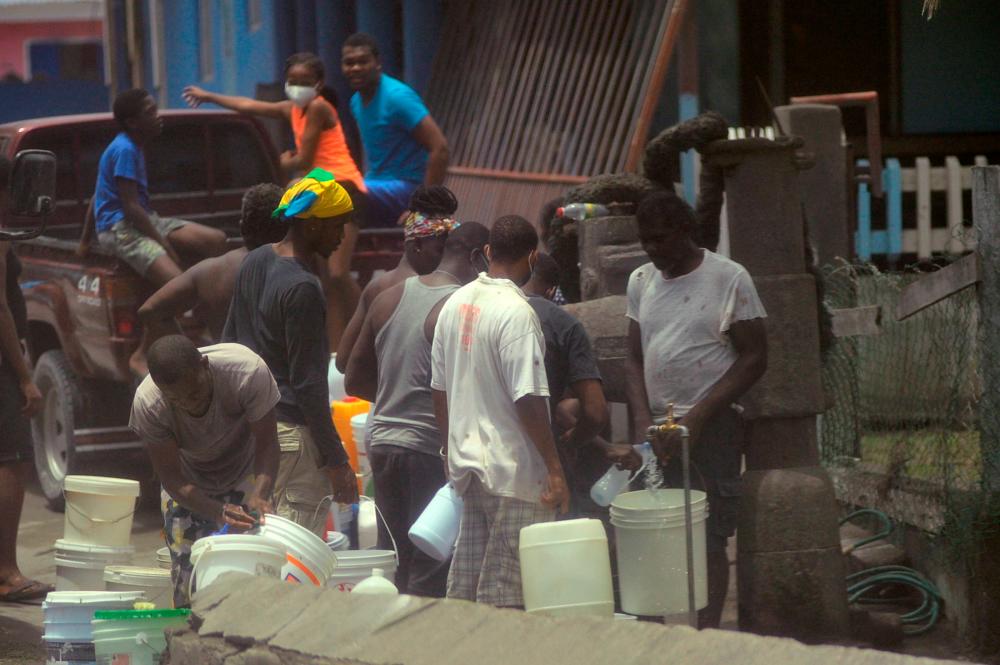 Local residents fill containers of water after a series of eruptions from La Soufriere volcano covered the area with a thick layer of ash in Biabou, Saint Vincent and the Grenadines, April 13, 2021. REUTERS/Robertson S. Henry