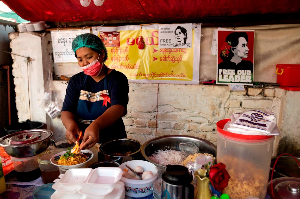 FILE PHOTO: A woman cooks at a food stall with posters against the military coup in Yangon, Myanmar, February 16, 2021. –Reuters