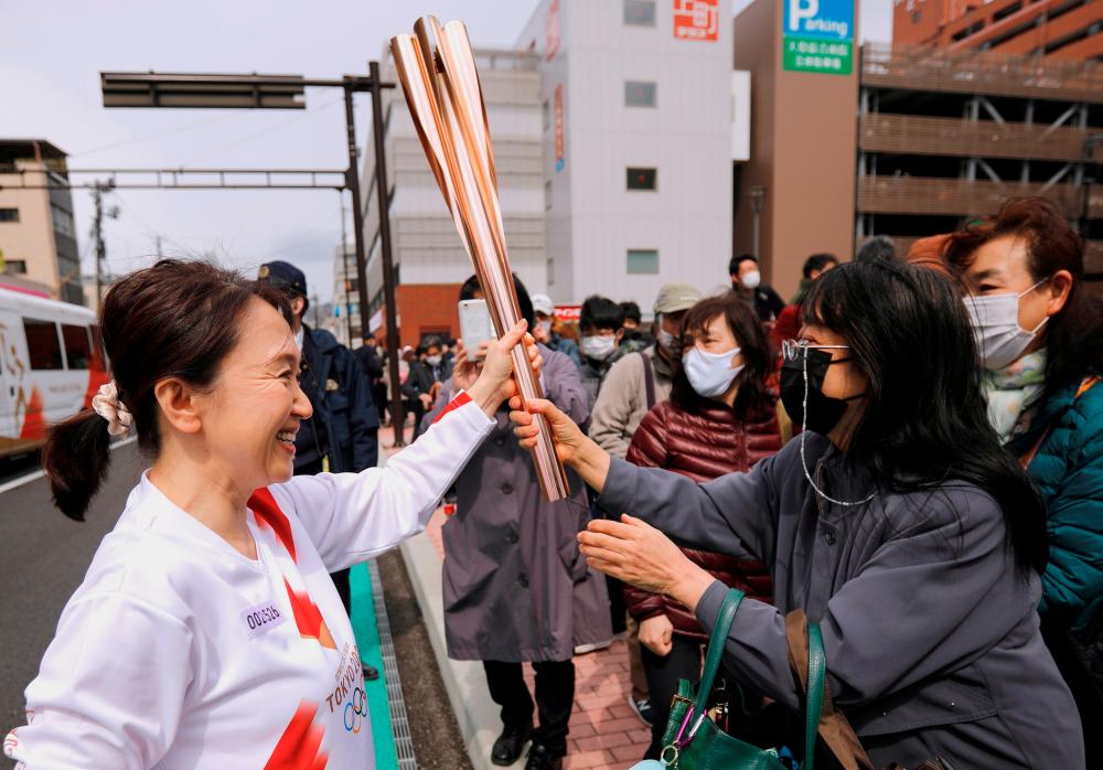 FILE PHOTO: Spectators try to touch the torch carried by torchbearer Junko Ito, after her run during the Tokyo 2020 Olympic torch relay on the second day of the relay in Fukushima, Japan March 26, 2021. - Reuters
