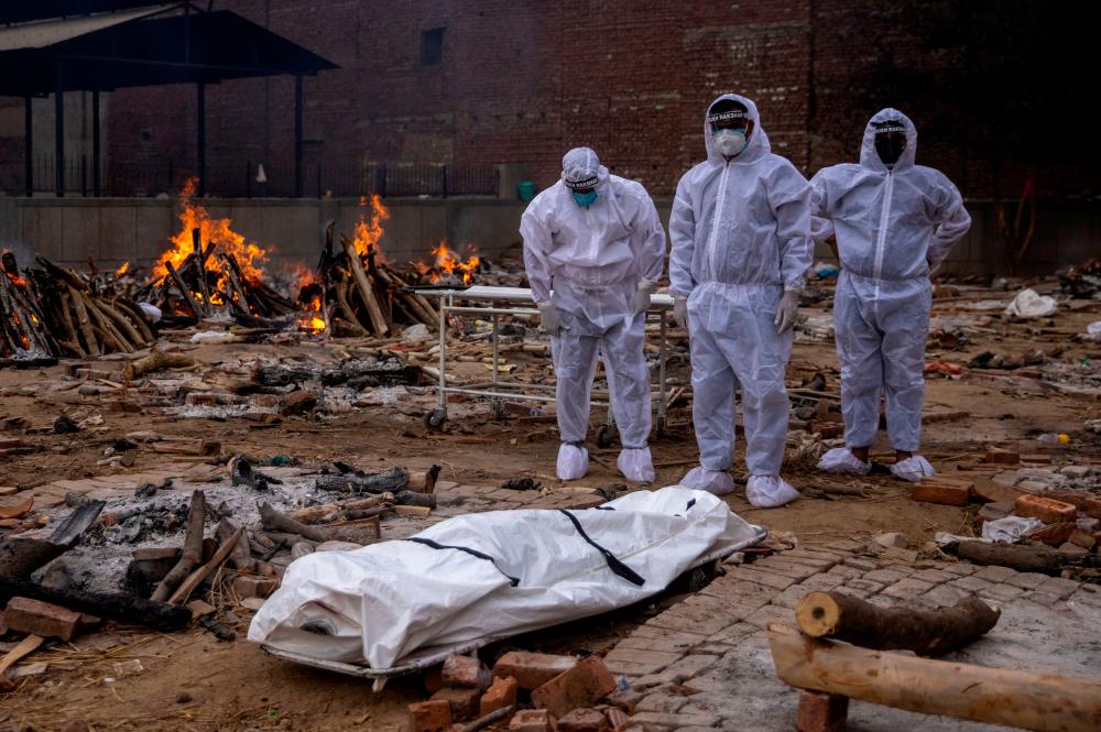 Men wearing protective suits stand next to the body of their relative, who died from the coronavirus disease (COVID-19), before her cremation at a crematorium ground in New Delhi, India, May 4, 2021. –Reuters