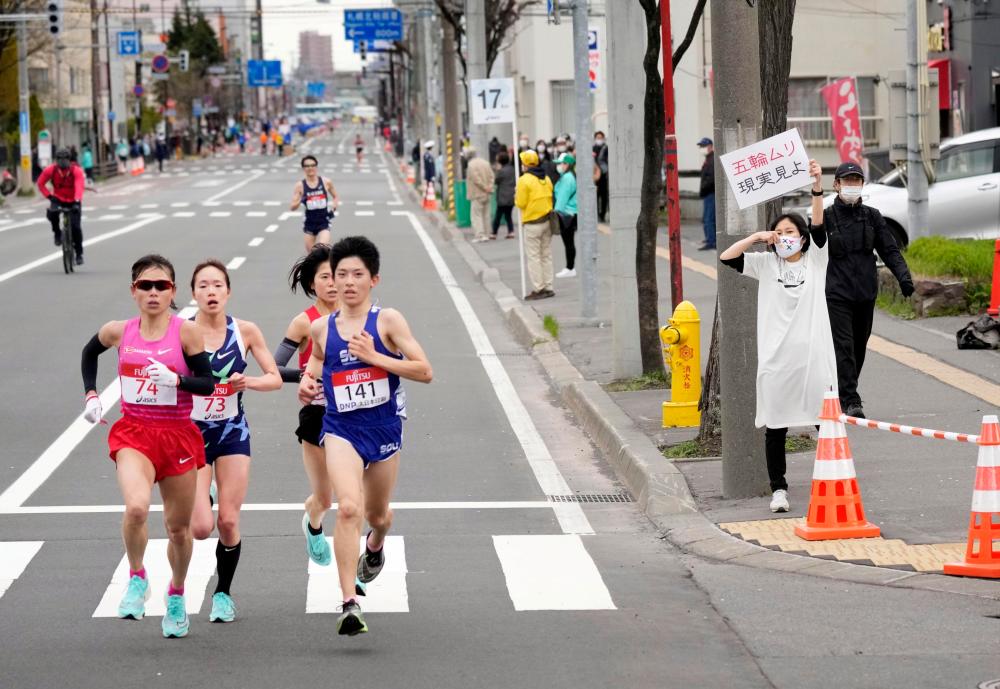FILE PHOTO: A spectator raises a paper sign reading ‘It is impossible to hold the Olympics, face up to reality’ along the race route during the half-marathon as part of Hokkaido-Sapporo Marathon Festival 2021, a testing event for the Tokyo 2020 Olympics marathon race.-Kyodo/via Reuters