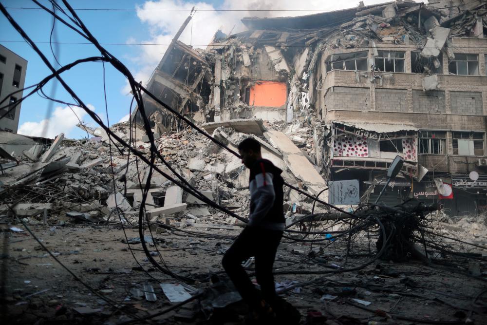 A Palestinian man walks past the remains of a tower building which was destroyed in Israeli air strikes, amid a flare-up of Israeli-Palestinian violence, on the first day of Eid al-Fitr holiday, in Gaza City May 13, 2021. - Reuters