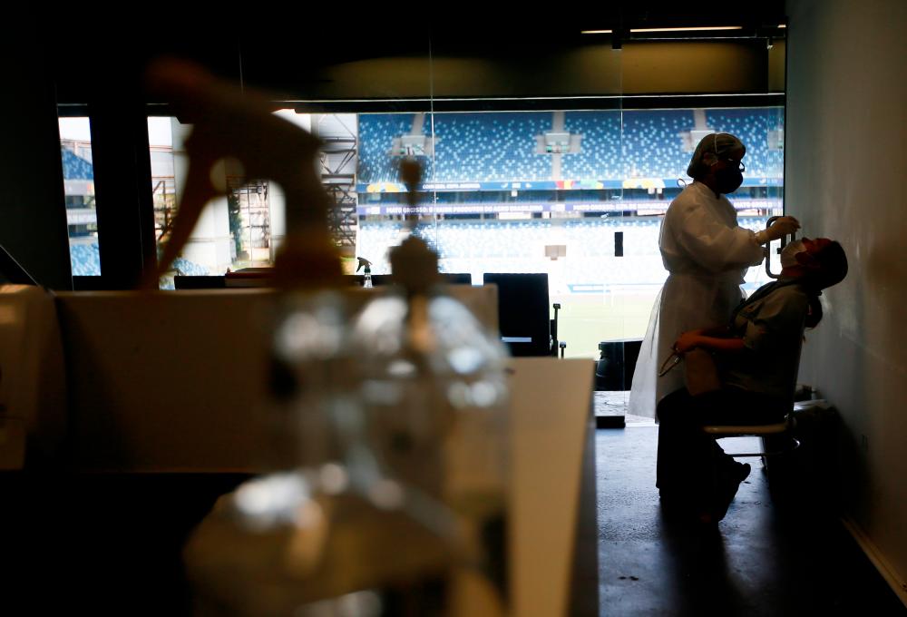 A health care worker performs a PCR test for Covid-19 to a worker of Arena Pantanal, for the Copa America.- Reuters