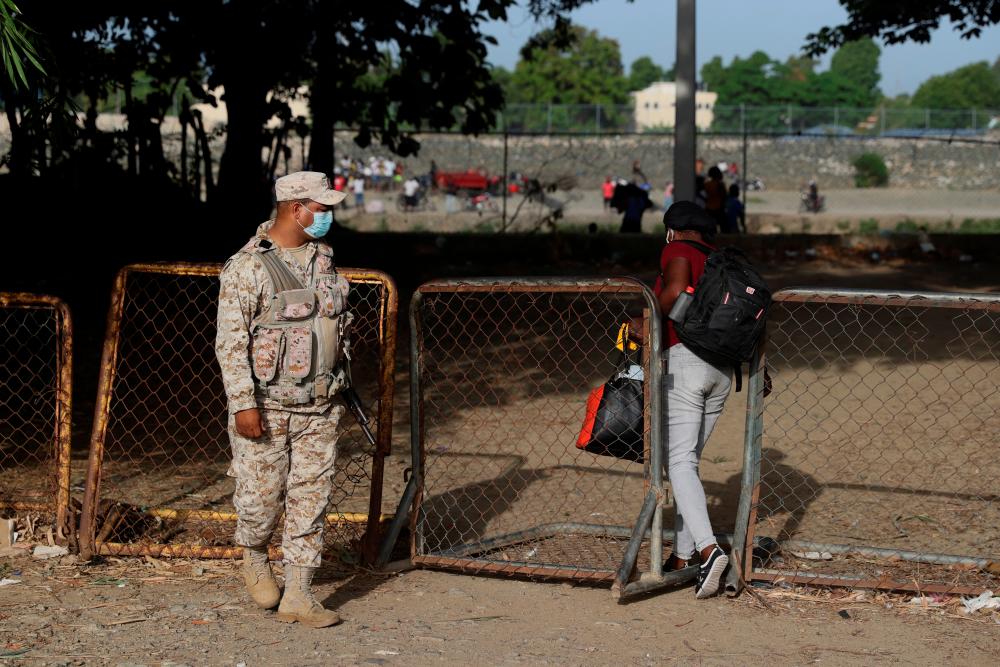 A member of the National Army observes an Haitian woman crossing a gate to head towards Haiti’s Ouanaminthe after the closing of the bridge between the Dominican Republic and Haiti following the killing of Haiti’s President Jovenel Moise, who was shot dead by gunmen at his private home in Port-au-Prince, in Dajabon, Dominican Republic July 8, 2021. -Reuters