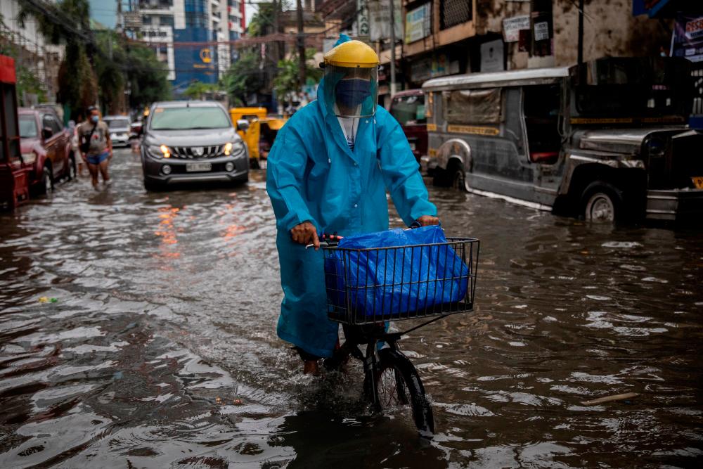 FILE PHOTO: A man wearing a face shield for protection against the coronavirus disease (COVID-19) rides a bicycle on a flooded street in Manila, Philippines, July 21, 2021. -Reuters