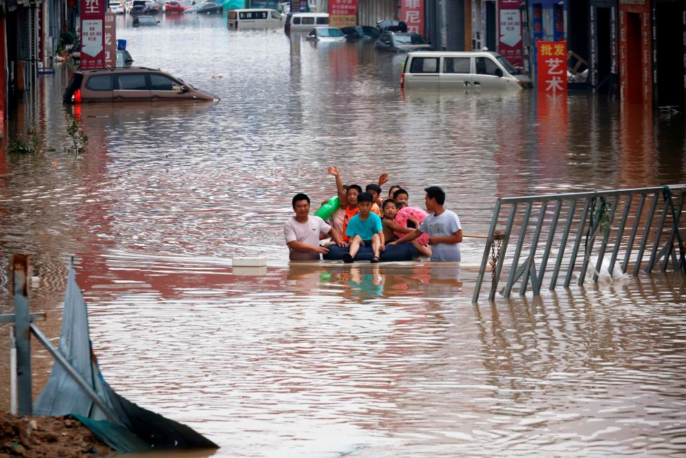 FILE PHOTO: Children sit on a makeshift raft on a flooded road following heavy rainfall in Zhengzhou, Henan province, China July 22, 2021. -Reuters