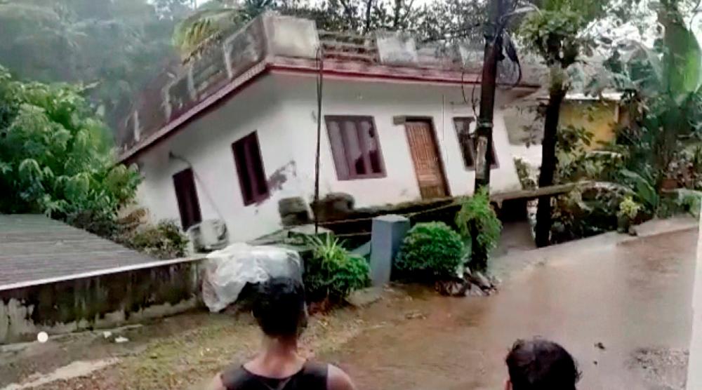 People watch a house being washed away in river due to strong current after heavy rains at Kottayam in Kerala, India, October 17, 2021 in this still image taken from video on October 18, 2021. REUTERSpix