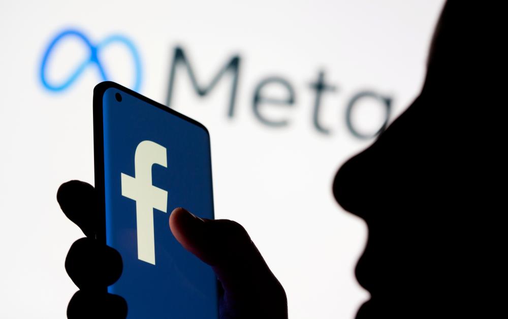 FILE PHOTO: FILE PHOTO: Woman holds smartphone with Facebook logo in front of a displayed Facebook's new rebrand logo Meta in this illustration picture taken October 28, 2021. REUTERSpix
