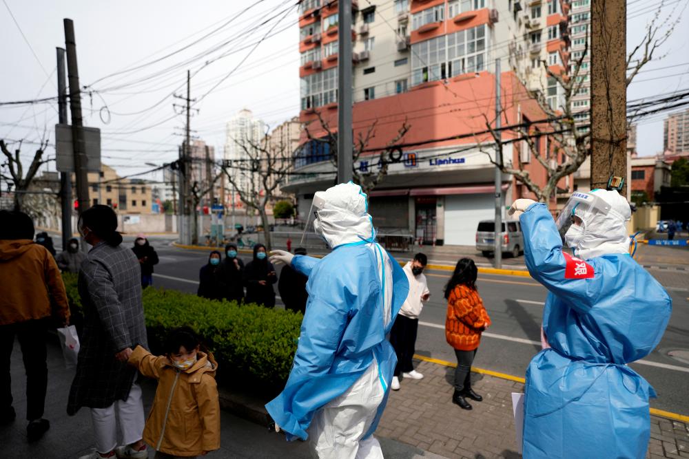 Workers in protective suits are seen next to residents lining up for nucleic acid testing, as the second stage of a two-stage lockdown to curb the spread of the coronavirus disease (Covid-19) begins in Shanghai, China April 1, 2022. REUTERSpix