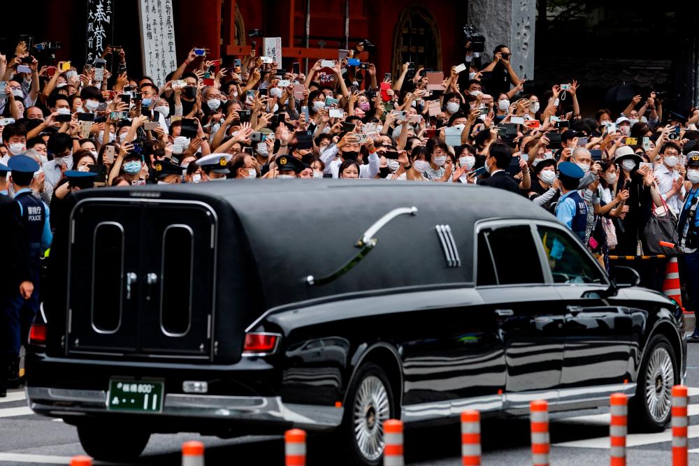 People watch as a vehicle carrying the body of the late former Japanese Prime Minister Shinzo Abe, who was shot while campaigning for a parliamentary election, leaves after his funeral at Zojoji Temple in Tokyo, Japan July 12, 2022/REUTERSPix