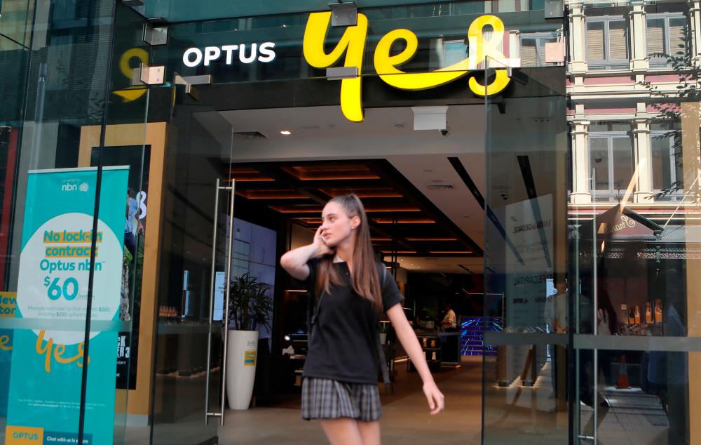 FILE PHOTO: A woman uses her mobile phone as she walks past in front of an Optus shop in Sydney, Australia, February 8, 2018. REUTERSPIX