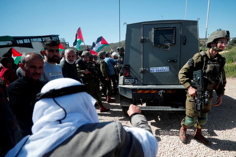Israeli forces stand guard near their vehicle as Palestinians protest against a new Israeli settlement near Ramallah in the Israeli-occupied West Bank, March 10, 2023. - REUTERSPIX