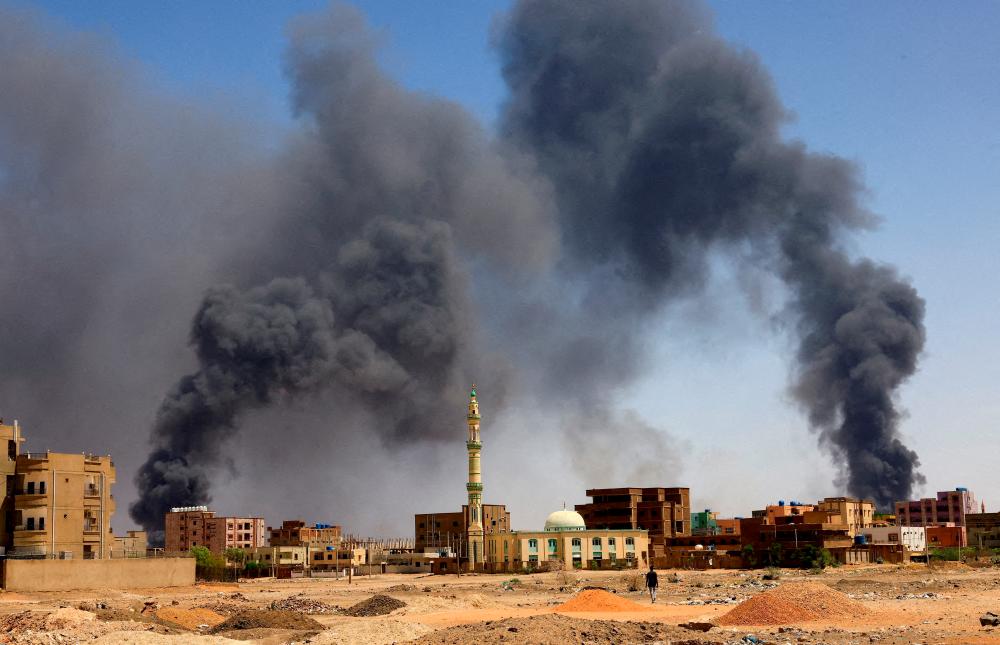 A man walks while smoke rises above buildings after aerial bombardment, during clashes between the paramilitary Rapid Support Forces and the army in Khartoum North, Sudan, May 1, 2023/REUTERSPix