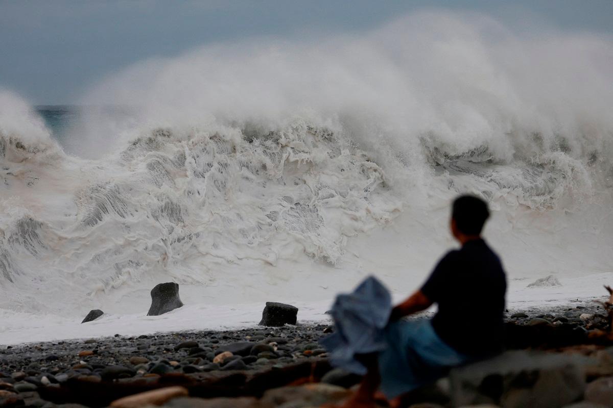 A woman sits by the shore while looking at waves breaking as Typhoon Koinu approaches, in Taitung, Taiwan October 4, 2023. - REUTERS/Carlos Garcia Rawlins
