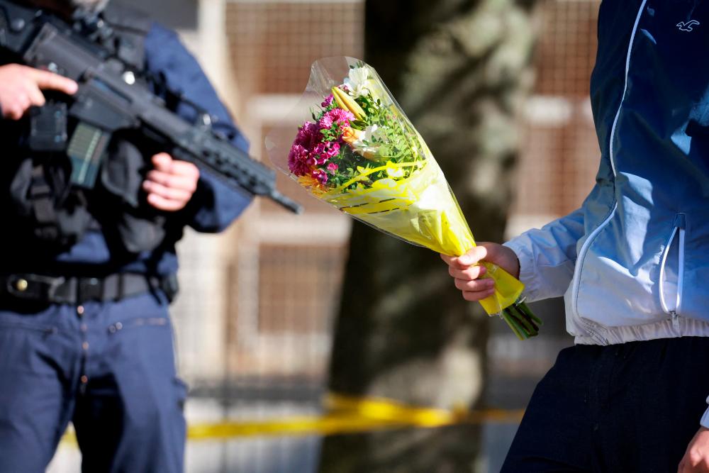 Police officers stand guard as people bring flowers in front of the Gambetta-Carnot school after French teacher Dominique Bernard was killed in a knife attack, in Arras, northern France, October 15, 2023. REUTERSPIX