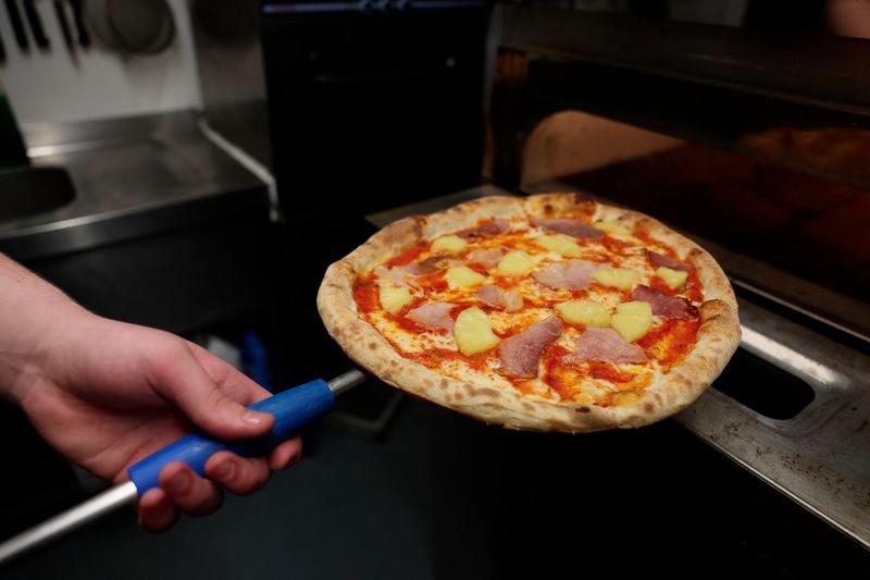 Chef Oliver Bardwell prepares a Hawaiian, ham, and pineapple-topped pizza at Lupa Pizza restaurant in Norwich, Britain, January 23, 2025. - REUTERSPIX