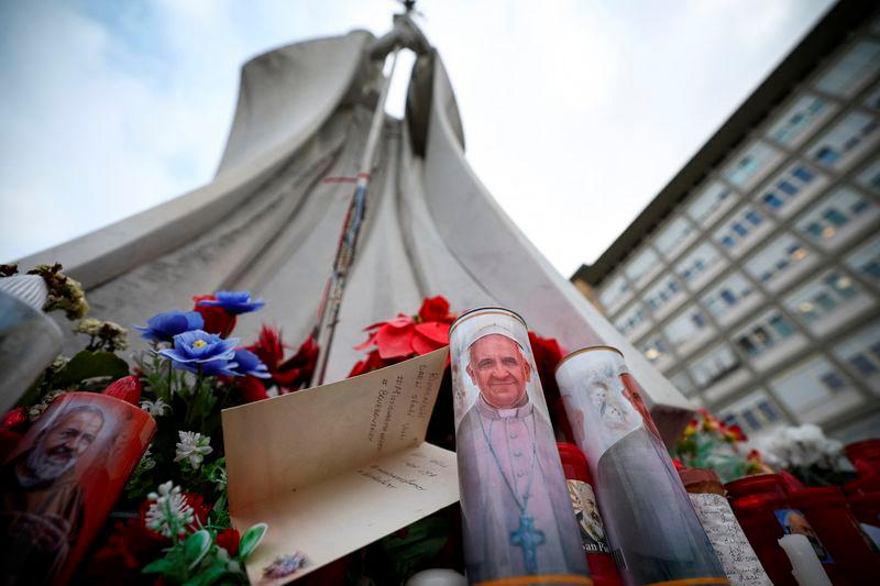 A candle with an image of Pope Francis and a card lie near the statue of the late Pope John Paul II outside the Gemelli Hospital, where Pope Francis is admitted to continue treatment for his ongoing respiratory tract infection, in Rome - REUTERSpix