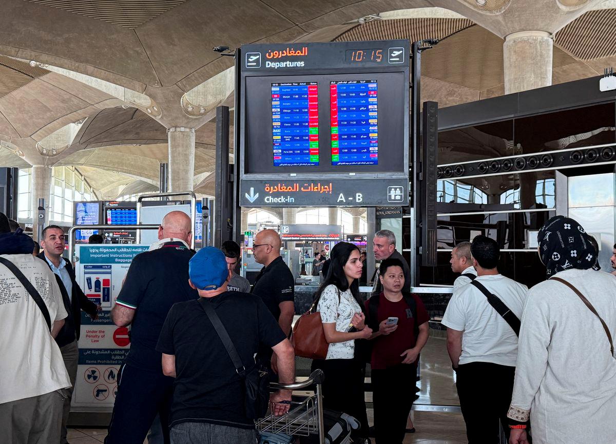 People stand in front of a flight information display screen showing information about delayed and cancelled flights, at Queen Alia International Airport in Amman, Jordan June 13, 2025. - REUTERSPIX