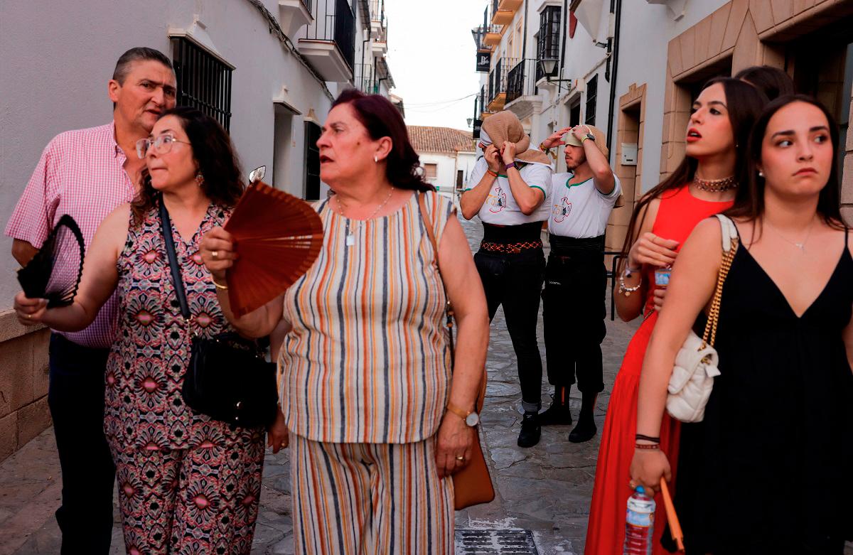 Faithful use hand fans to cool off next to ‘costaleros’, men who carry a structure traditionally known as ‘paso’, bearing the statues of Christ and the Virgin, during the first summer heatwave in Ronda, Spain, June 28, 2025. REUTERS/Jon Nazca