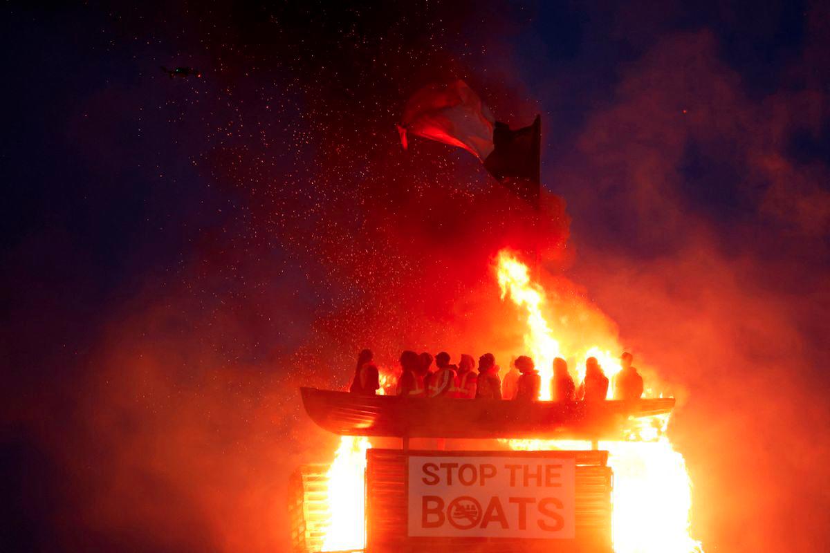 A loyalist bonfire burns after being set alight, featuring a model effigy of a boat containing mannequins portrayed as migrants in lifejackets, with a sign reading Stop the Boats, during annual bonfire events marking the 1690 Battle of the Boyne, in Moygashel, Northern Ireland, July 10, 2025. - REUTERSPIX