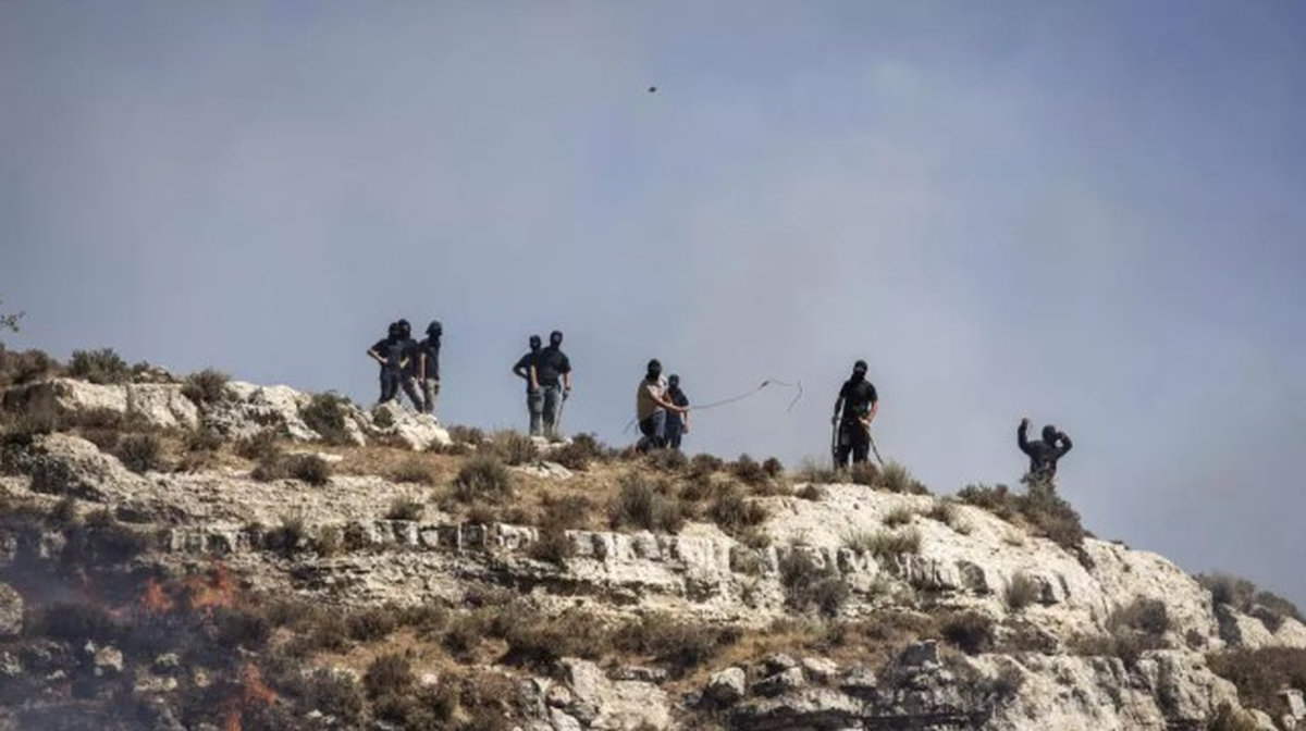 Masked Israeli settlers hurl rocks at Palestinians from hilltop in the West Bank village of Sinjil on July 4, 2025. - AFP