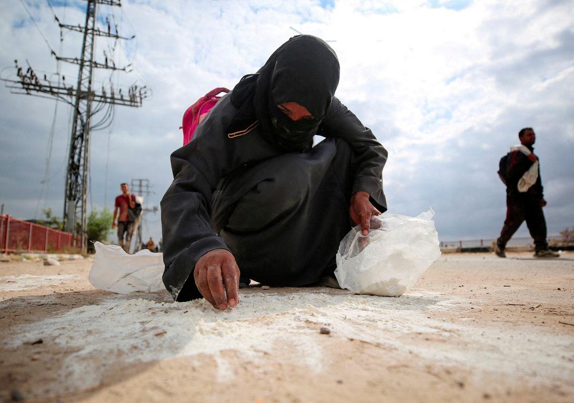 A woman collects flour from the ground as Palestinians receive aid supplies from the U.S.-backed Gaza Humanitarian Foundation (GHF), in the central Gaza Strip, August 1, 2025. - REUTERSPIX