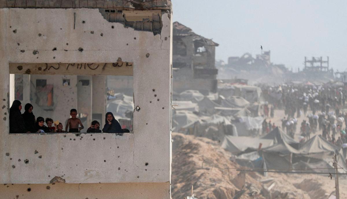 Wanita dan kanak-kanak melihat dari bangunan yang rosak ketika penduduk Palestin membawa bekalan bantuan yang memasuki Gaza melalui Israel, di Beit Lahia, utara Semenanjung Gaza, 2 Ogos 2025 - REUTERS/Mahmoud Issa TPX IMAGES OF THE DAY