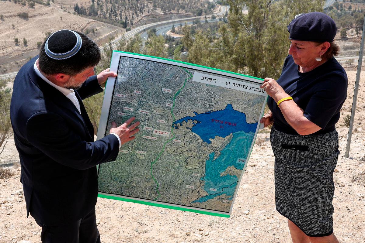 Israeli Finance Minister Bezalel Smotrich and a woman hold a map that shows the long-frozen E1 settlement scheme, that would split East Jerusalem from the occupied West Bank, on the day of a press conference near the Israeli settlement of Maale Adumim, in the Israeli-occupied West Bank, August 14, 2025. - REUTERSPIX