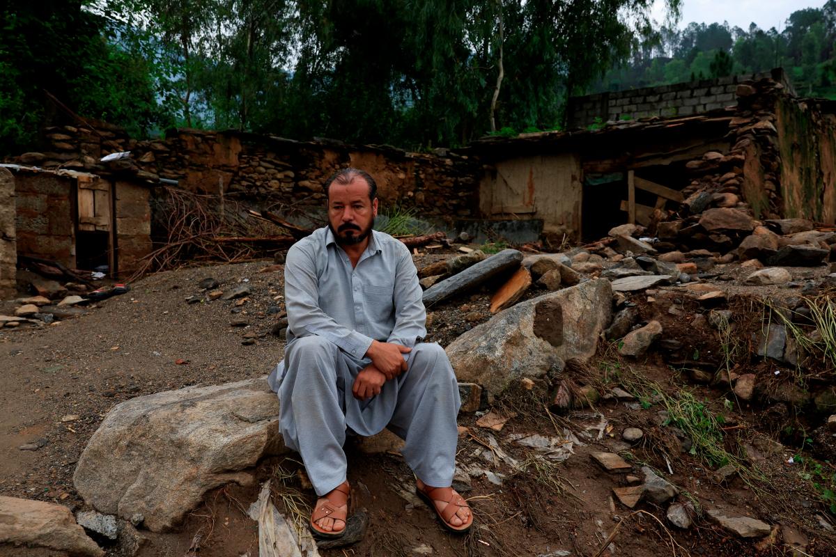 Aziz Ahmed, 45, a school teacher, sits with a damaged house in the background following a storm that caused heavy rains and flooding, in Bayshonai Kalay, Buner district, Khyber Pakhtunkhwa province, Pakistan, August 17, 2025. REUTERS/Akhtar Soomro