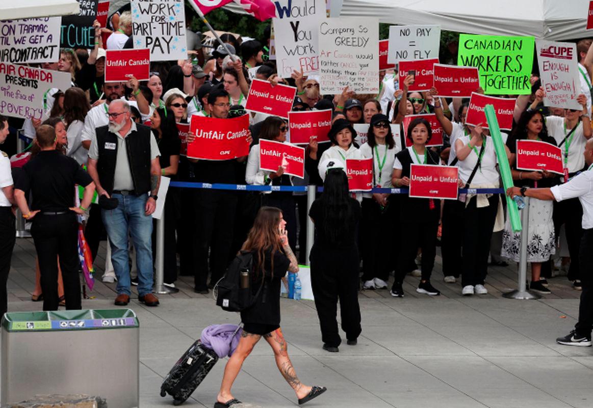 A passenger walks as striking Air Canada flight attendants hold placards as they defy a back to work order at Vancouver International Airport in Richmond, British Columbia, Canada August 18, 2025. - REUTERSPIX