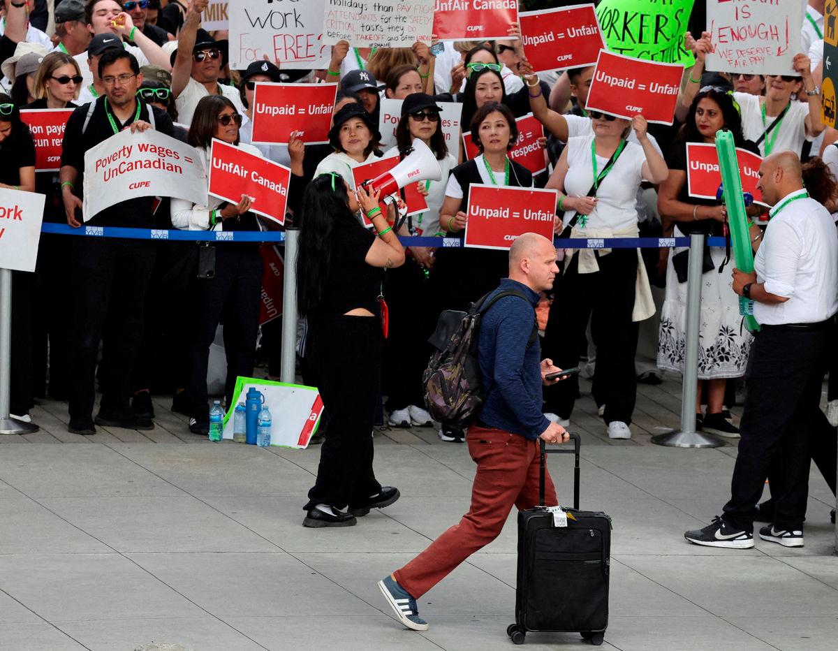 FILE PHOTO: A passenger walks as striking Air Canada flight attendants hold placards as they defy a back to work order at Vancouver International Airport in Richmond, British Columbia, Canada August 18, 2025. REUTERS/Chris Helgren/File Photo/File Photo