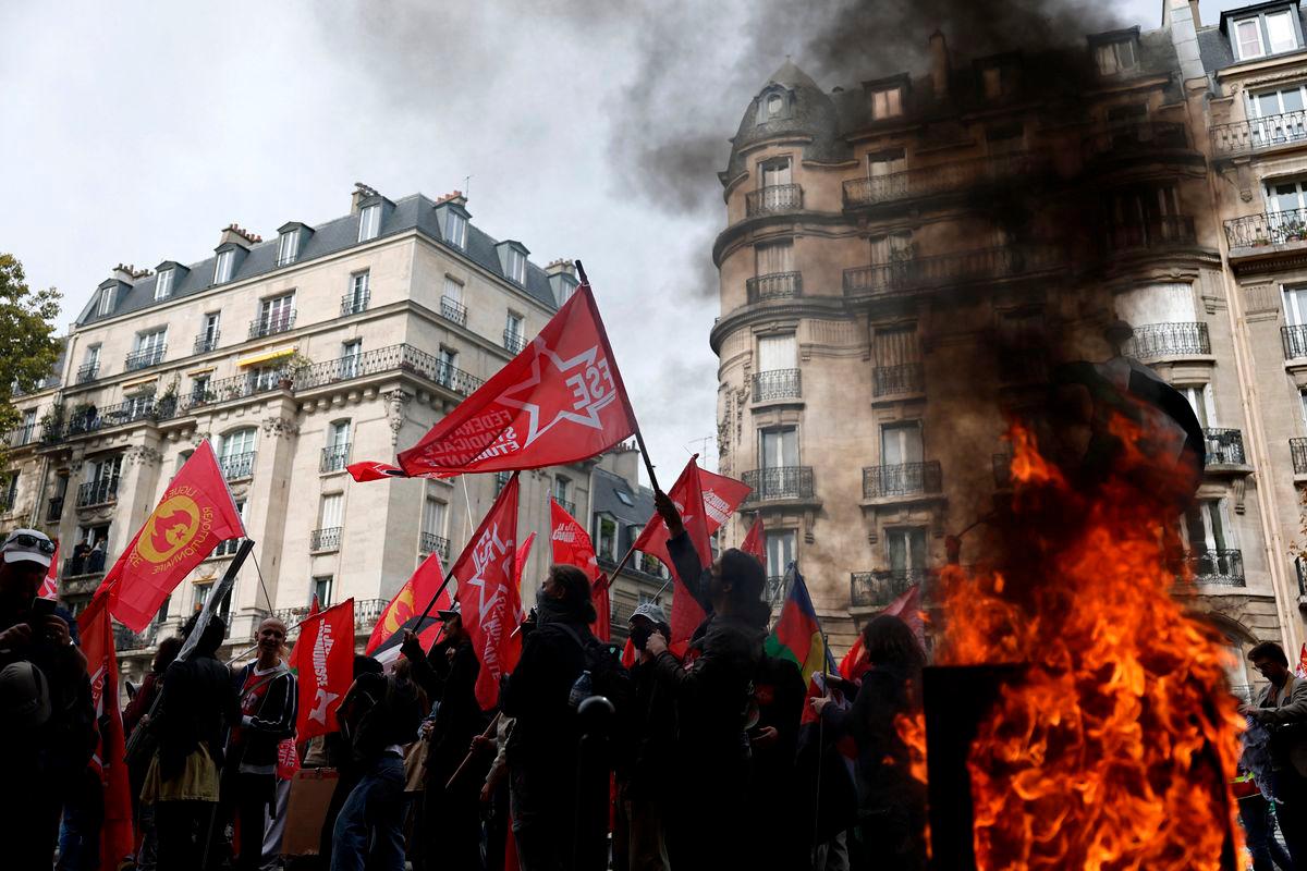 Protesters holding flags walk past a burning garbage bin during a demonstration in Paris as part of a day of nationwide strikes and protests against the government and possible austerity cuts in France, October 2, 2025. REUTERS/Benoit Tessier