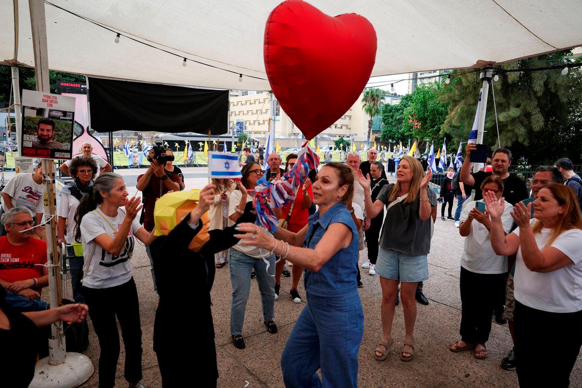 A person wearing a mask depicting U.S. President Donald Trump holds an Israeli flag and a heart-shaped ballon, as people celebrate after Trump announced that Israel and Hamas agreed on the first phase of a Gaza ceasefire, at the “Hostages square”, in Tel Aviv, Israel, October 9, 2025. REUTERS/Ronen Zvulun