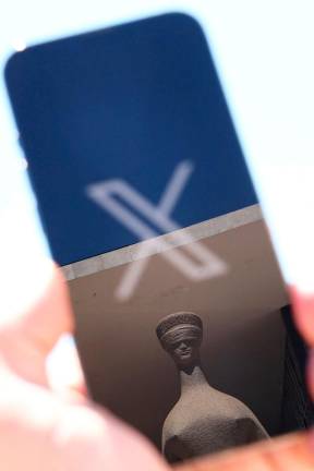 The logo of social media platform X is seen on a mobile phone next to a reflection of Alfredo Ceschiatti’s sculpture The Justice, outside Brazil’s Supreme Court in this illustration taken August 30, 2024, in Brasilia, Brazil. - REUTERSpix